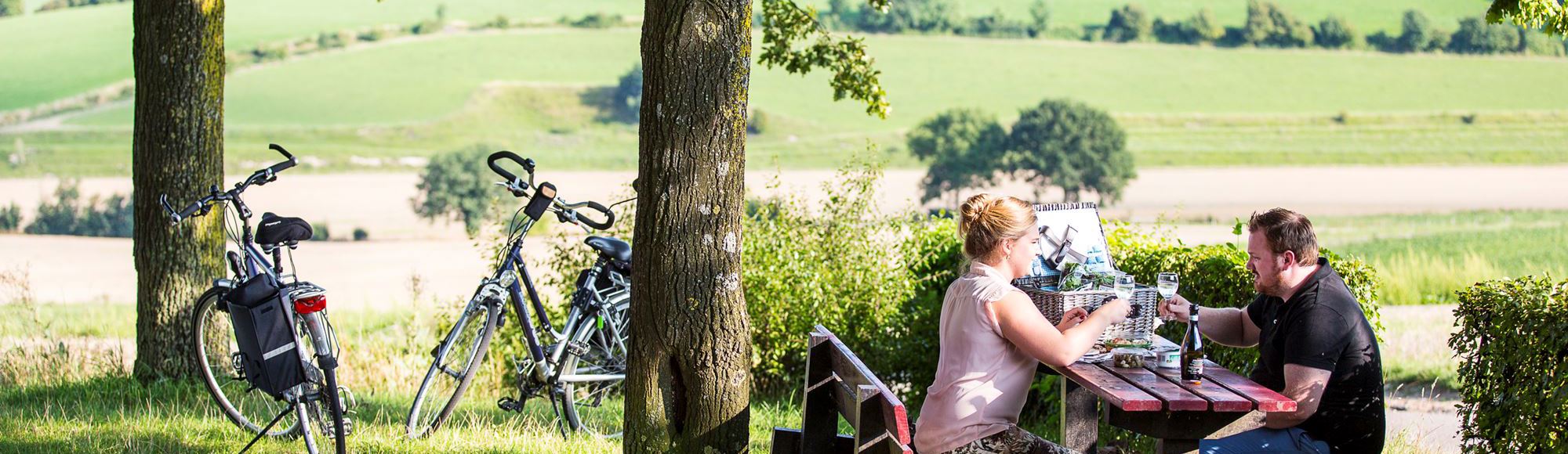Een man en een vrouw zitten aan een picknicktafel boven aan de Gulperberg met twee fietsen