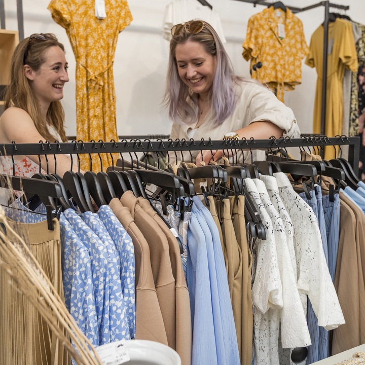 Twee vrienden kijken lachend tussen de kleding in een kledingrek
