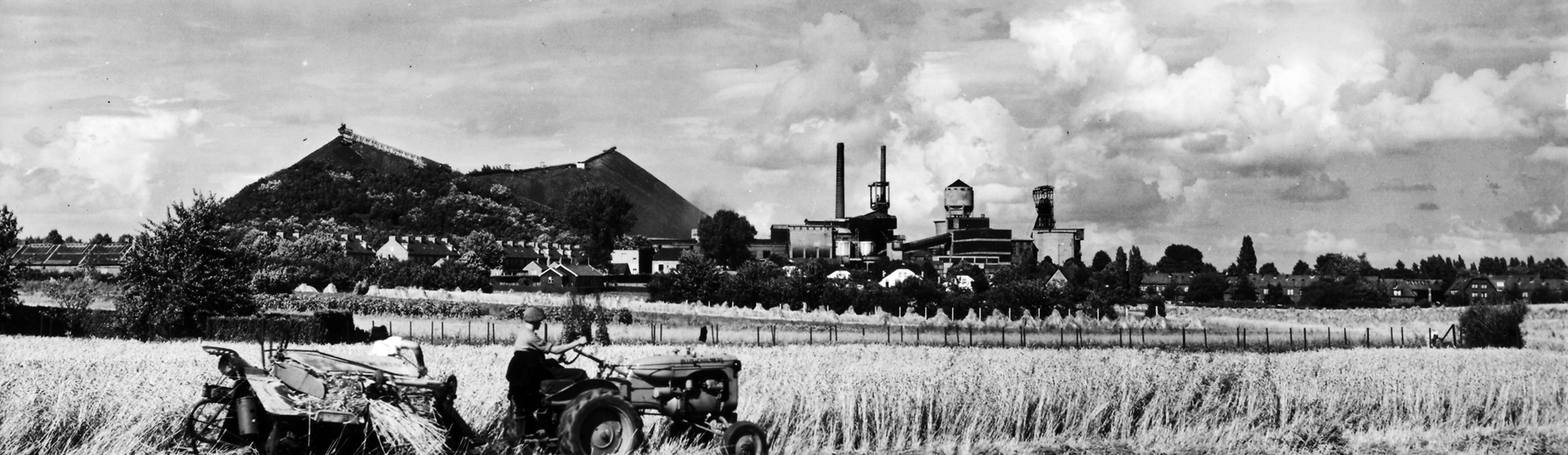 Een oude zwart-wit foto met zicht op de Wilhelmina mijn en berg, voorgrond een tractor.