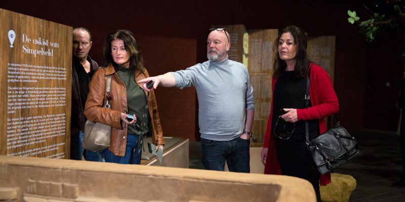 4 mensen waarvan er eentje wijst bij askist in Romeins Museum