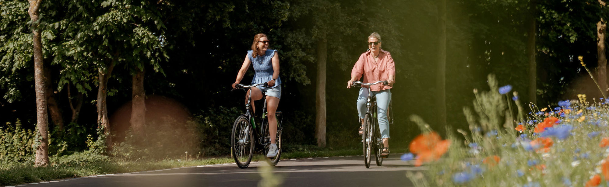 Twee dames op een zomerse dag fietsen over de Parkstadroute met bloemetjes langs de kant.