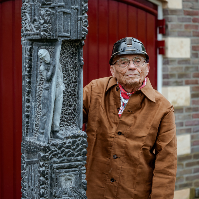 Oud-koempel leunt tegen monument voor de mijnwerkers.