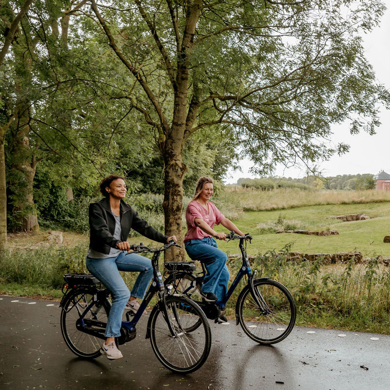 Twee dames fietsen vrolijk naast elkaar met uitzicht op Brasserie Nieuw Erenstein in Kerkrade.
